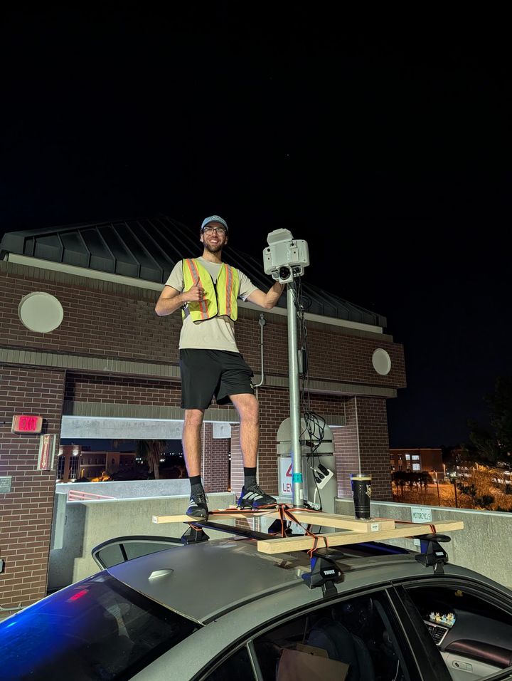 Benjamin on a parking garage roof at night beside the deployed crash detection unit on a pole